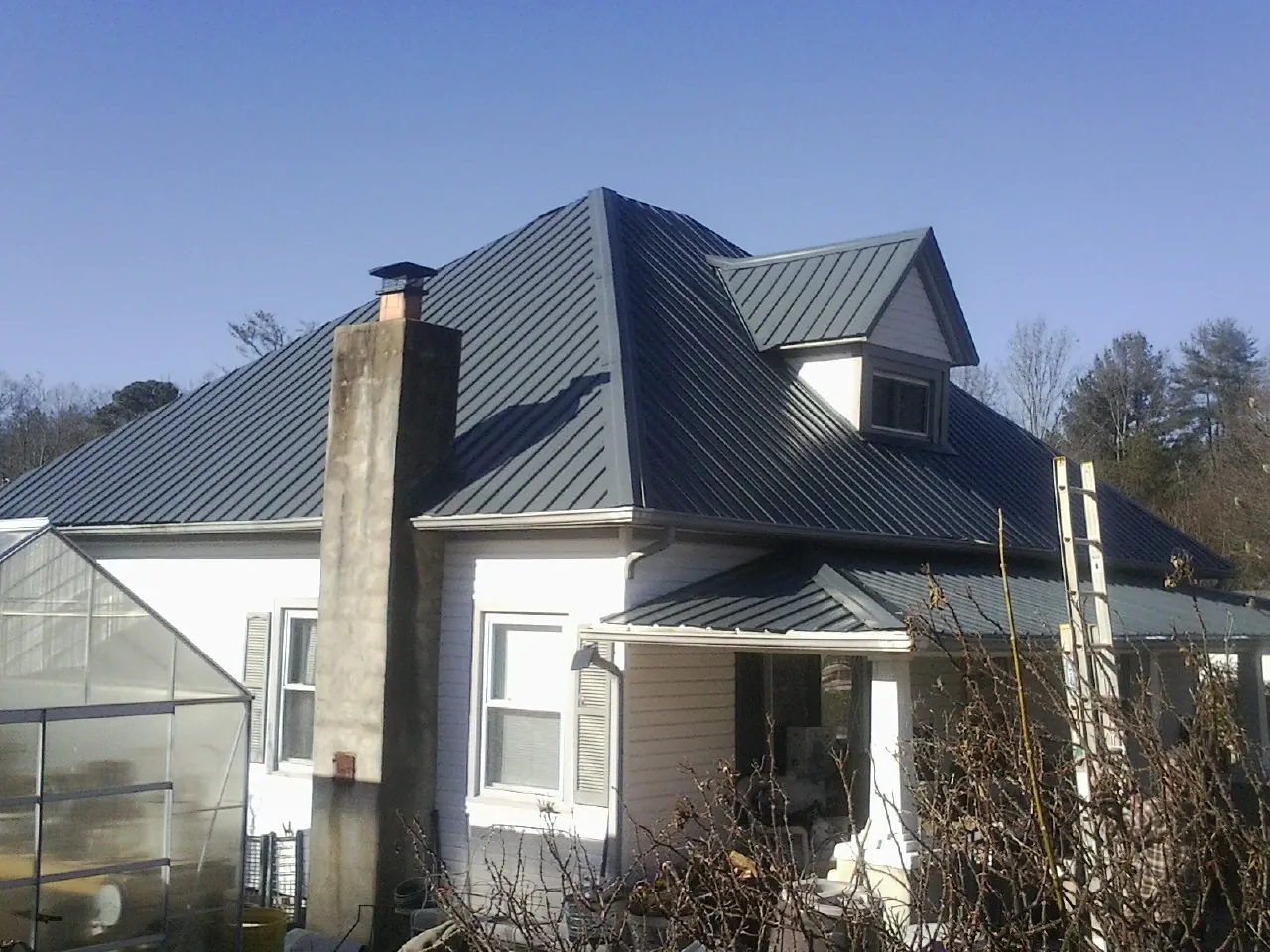 Dark blue standing seam metal roof on a white farmhouse with dormer — Slate & Tile Roof Repair by Roofing Brothers in Coinjock