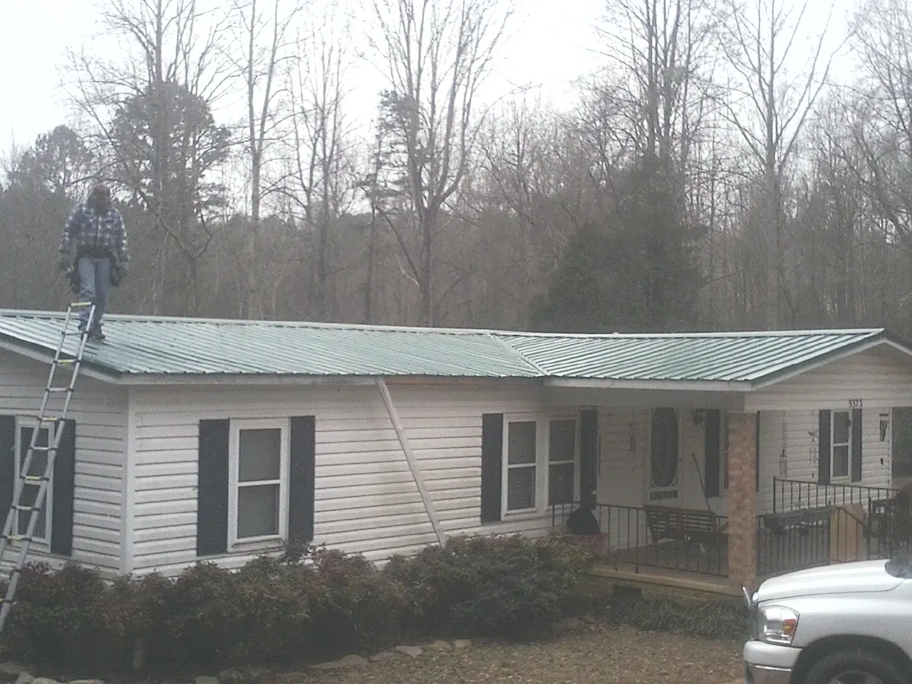 Worker on a ladder beside a new green metal roof on a ranch home in Coinjock