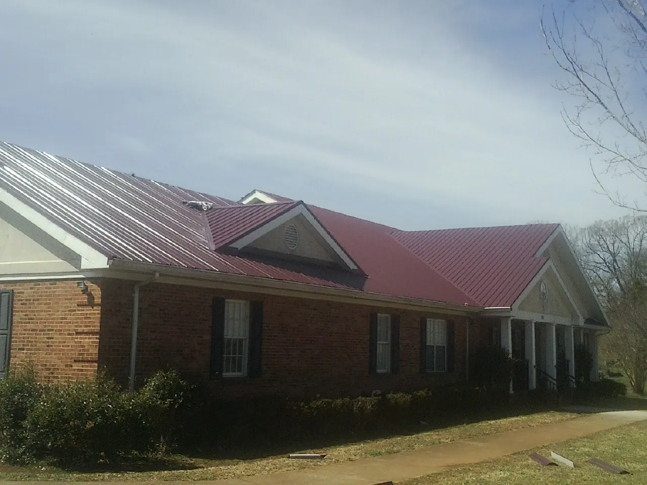 Red metal roof with gabled entries on a long brick building, from a Hail Damage Roof Repair job in Coinjock