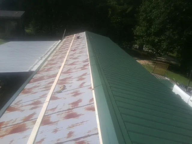 Old rusted panels beside newly installed green metal roofing — Wind Damage Roof Repair by Roofing Brothers in Coinjock