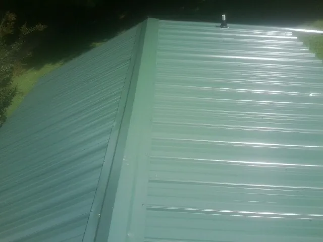 New green metal panels meeting at the ridge of a roof — Flat Roof Repair work by our crew in Coinjock