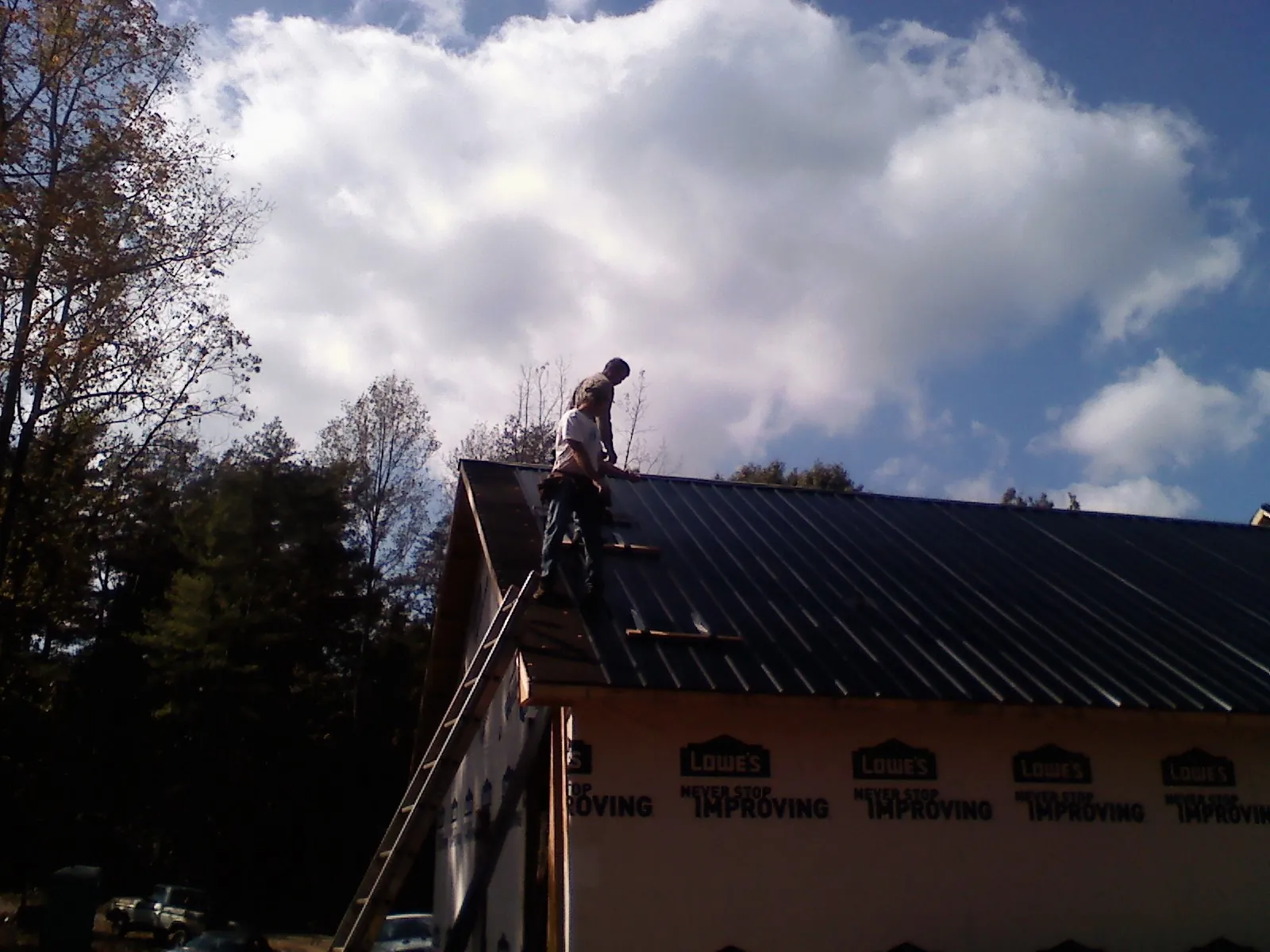 Roofer fastening dark metal panels high against a cloudy sky, from a Roof Inspection job in Coinjock
