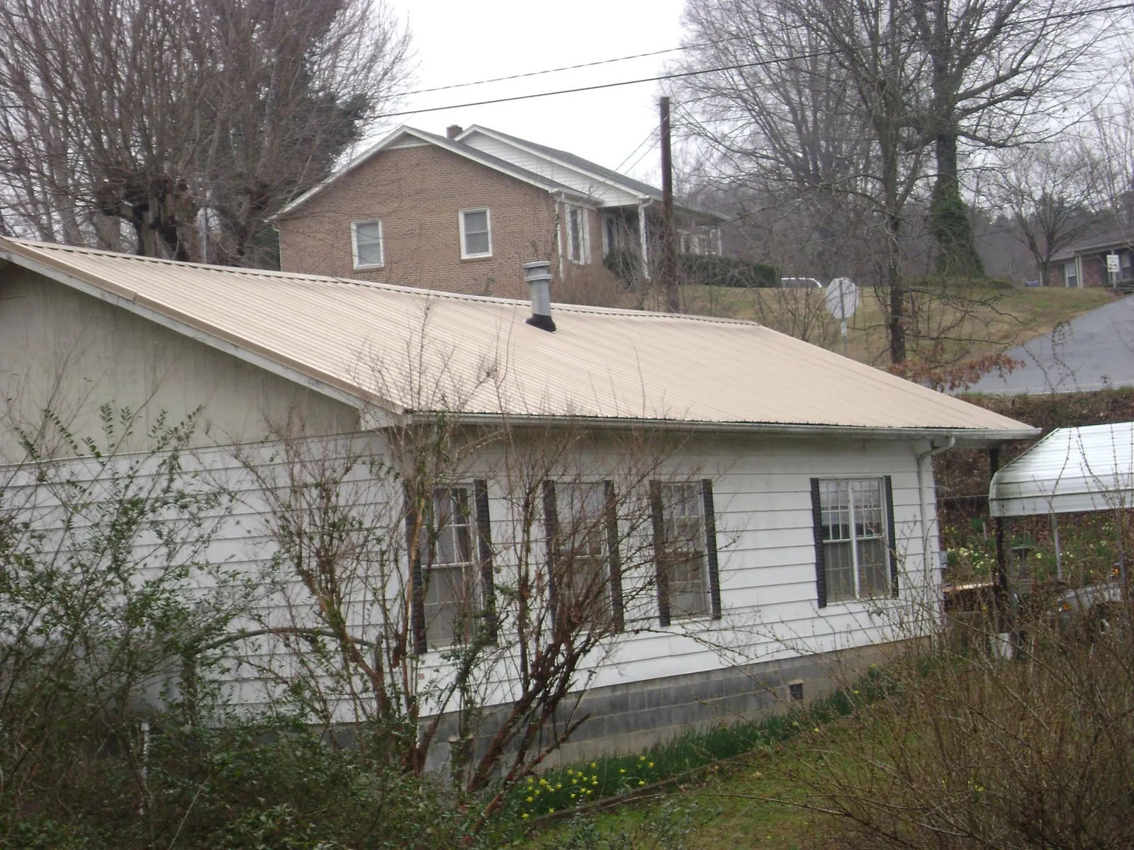 Tan metal roof on a white sided house set into a hillside — Commercial Roofing by Roofing Brothers in Coinjock